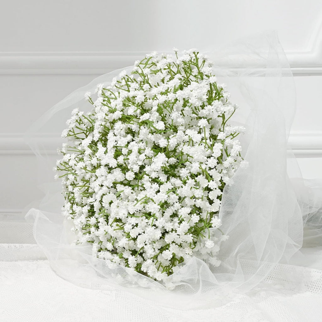 Bouquet of artificial white babys breath flowers wrapped in sheer white tulle, set against a white background with lace detail.