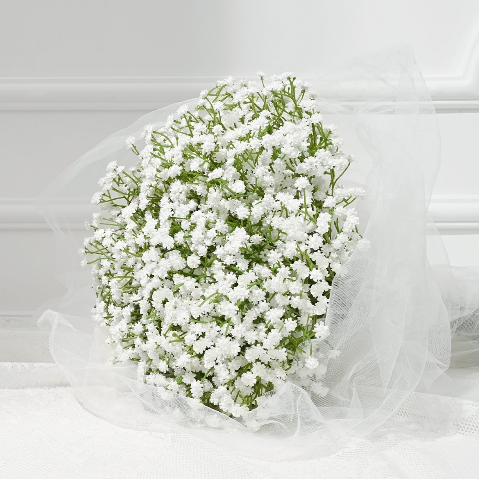 Bouquet of artificial white babys breath flowers wrapped in sheer white tulle, set against a white background with lace detail.