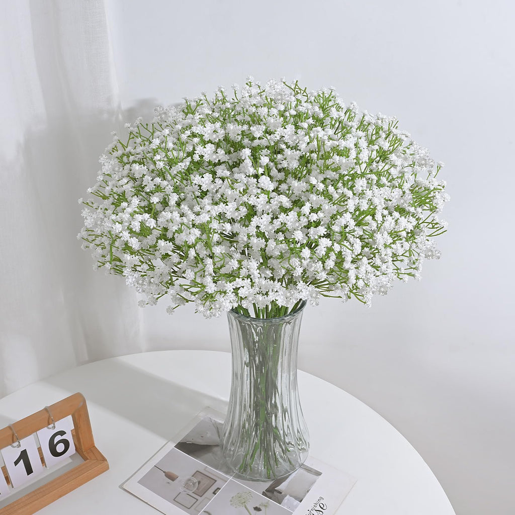 Artificial white babys breath flowers in a clear glass vase on a white table with a wooden calendar.