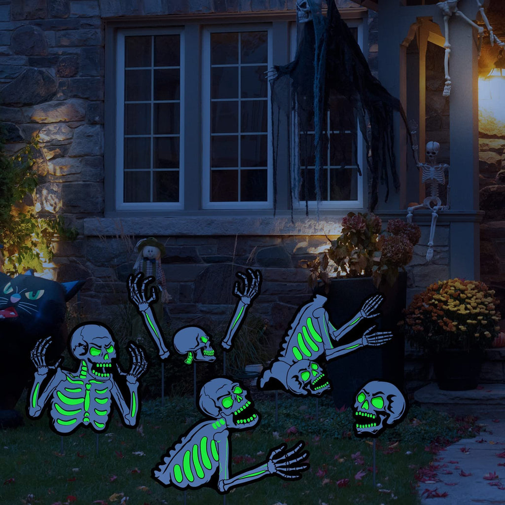 Fluorescent skeleton yard signs with glowing green eyes and ribs, displayed on a lawn at night in front of a house.