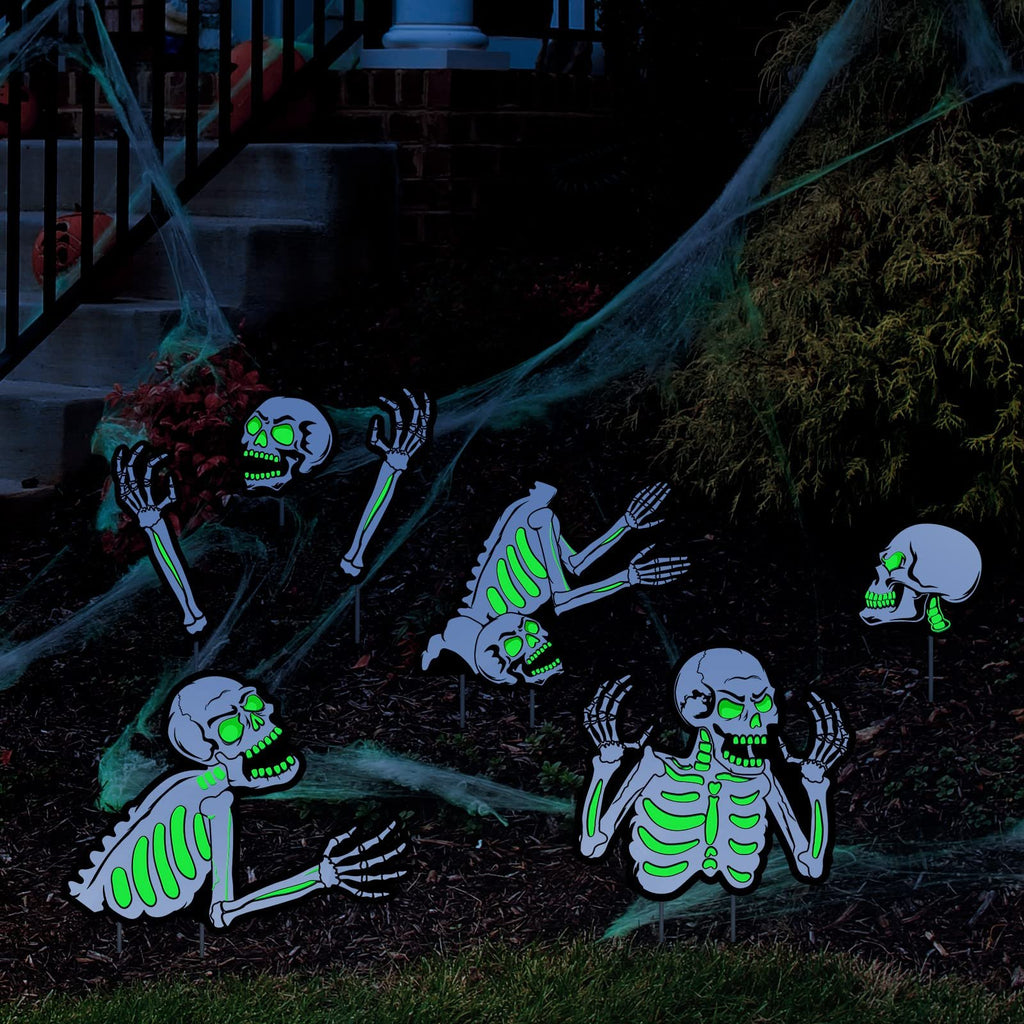 Fluorescent skeleton yard decorations with green glowing eyes and ribs, arranged on a lawn with cobwebs and near stairs.
