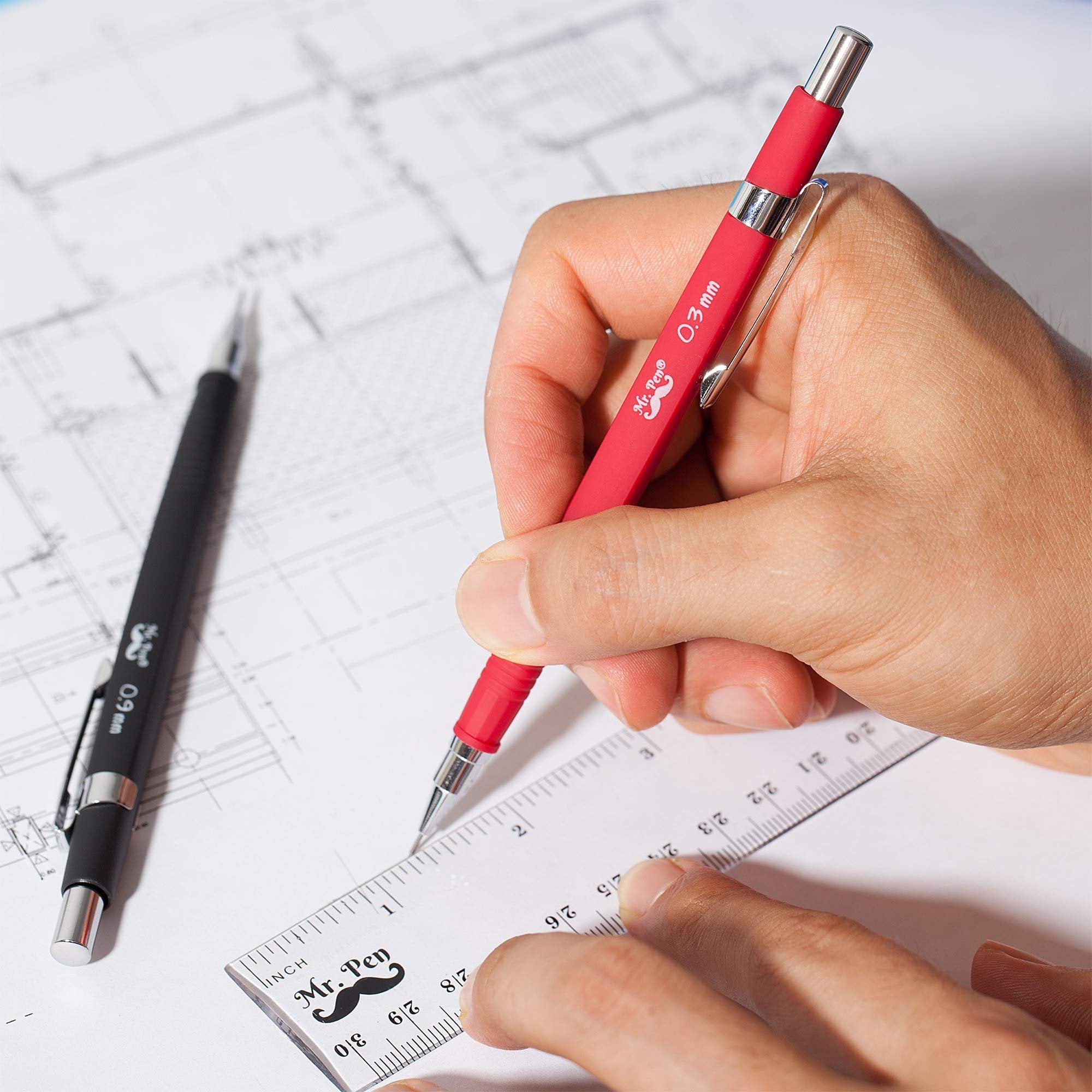 Hands using a red and black mechanical pencil set with a ruler on blueprints. The red pencil is labeled 0.3mm and the black pencil is labeled 0.9mm.