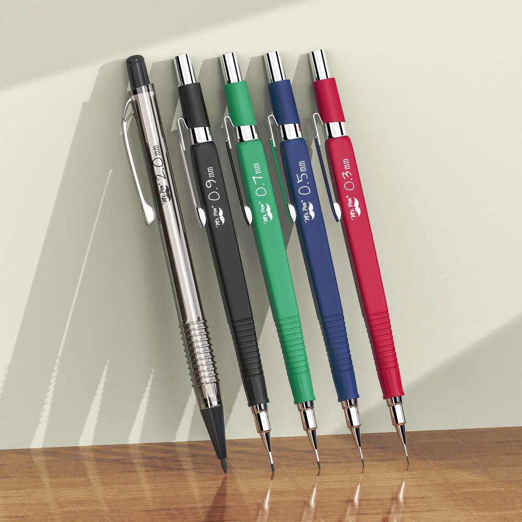 Five mechanical pencils in different colors and lead sizes, leaning against a wall on a wooden surface.