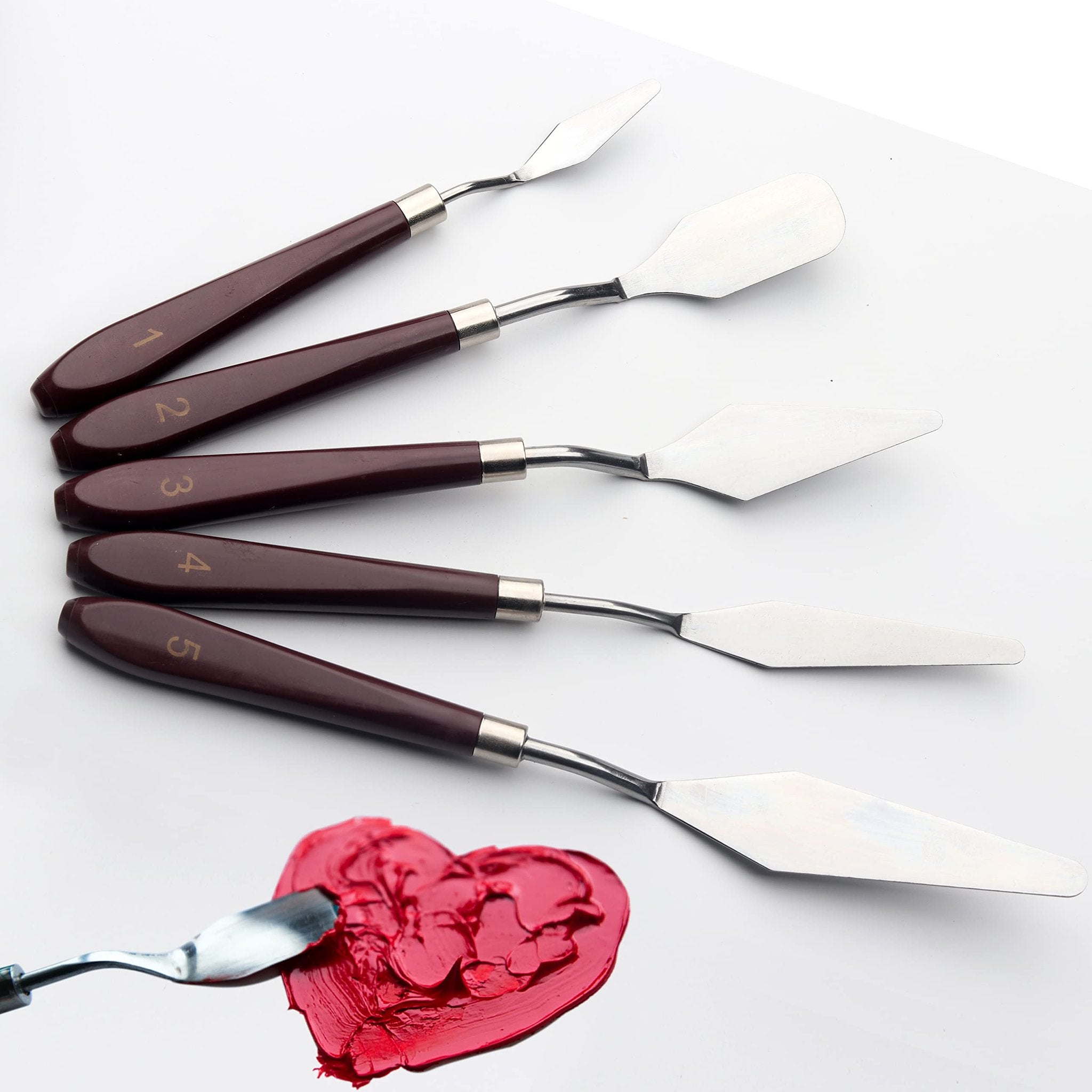 Five stainless steel palette knives with brown handles, numbered 1 through 5, arranged diagonally, with one knife spreading red paint in a heart shape.
