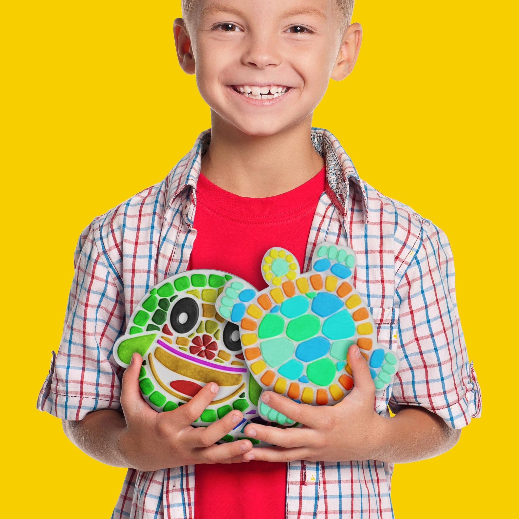 Smiling boy holding two colorful mosaic stepping stones, one shaped like a monster face, the other like a turtle.