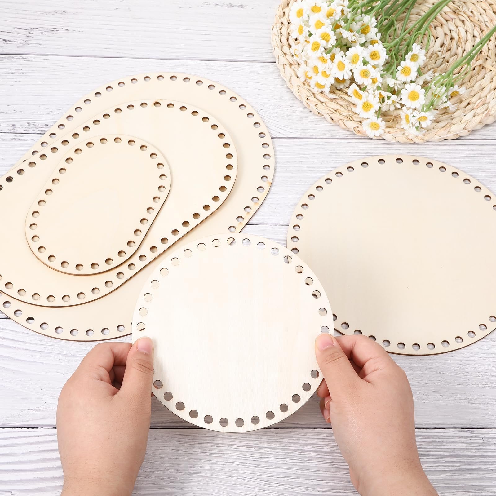 Hands holding assorted oval and round wooden basket bases with laser-cut holes for crafting