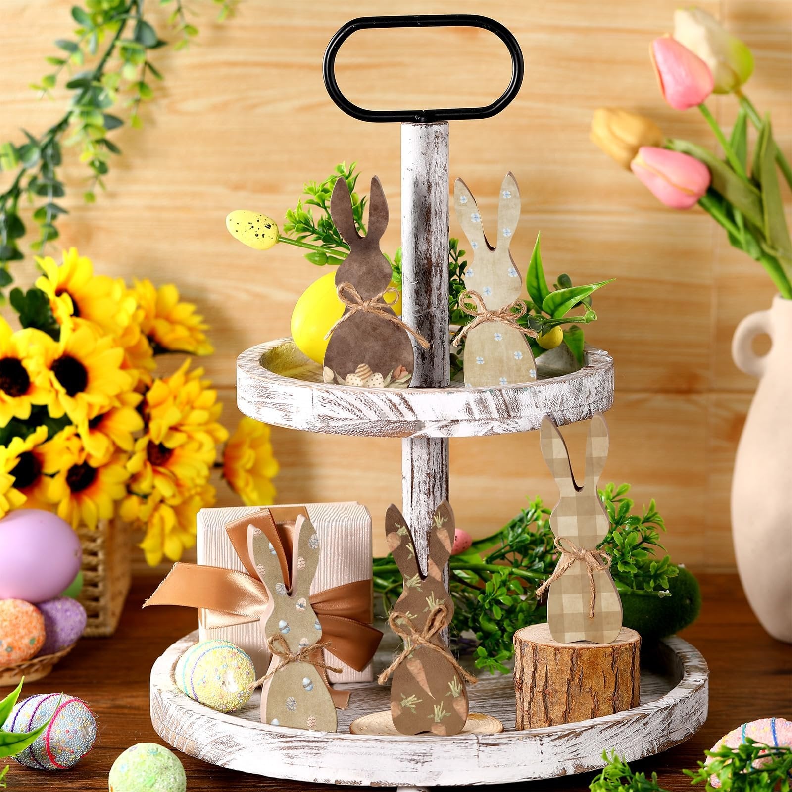 Tiered tray decorated with wooden Easter bunnies, sunflowers, tulips, and decorative eggs.