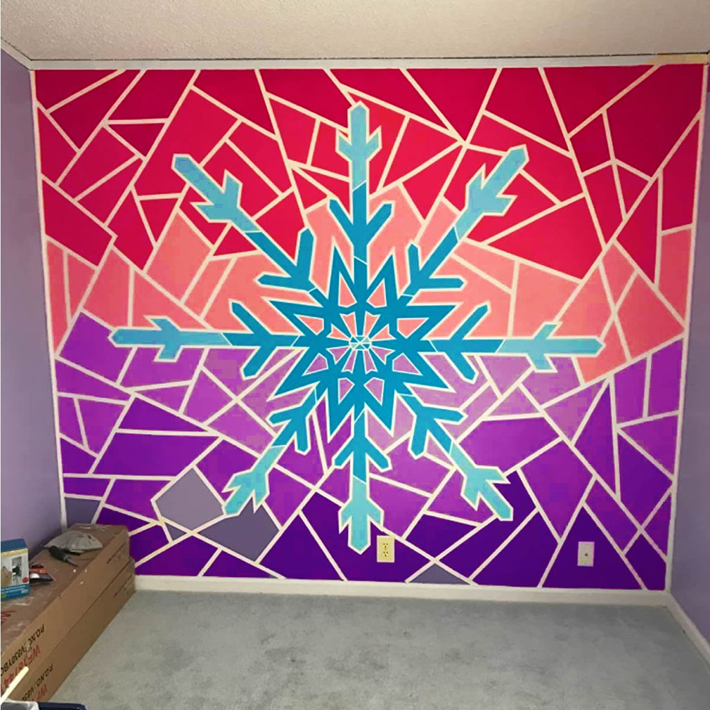 Wall mural with a large blue snowflake design on a gradient background of pink, purple, and red geometric shapes, outlined in white.