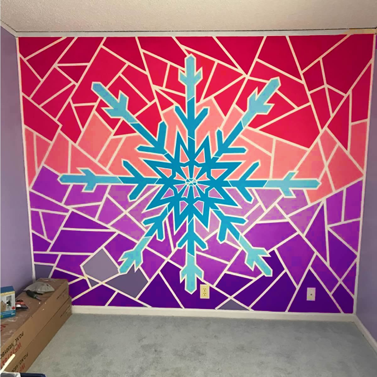 Wall mural with a large blue snowflake design on a gradient background of pink, purple, and red geometric shapes, outlined in white.