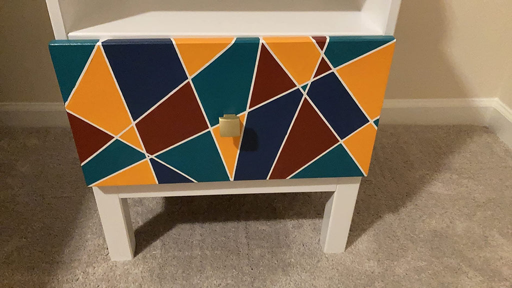 Drawer front with a geometric pattern of teal, orange, navy, and maroon shapes separated by white lines, with a gold knob.