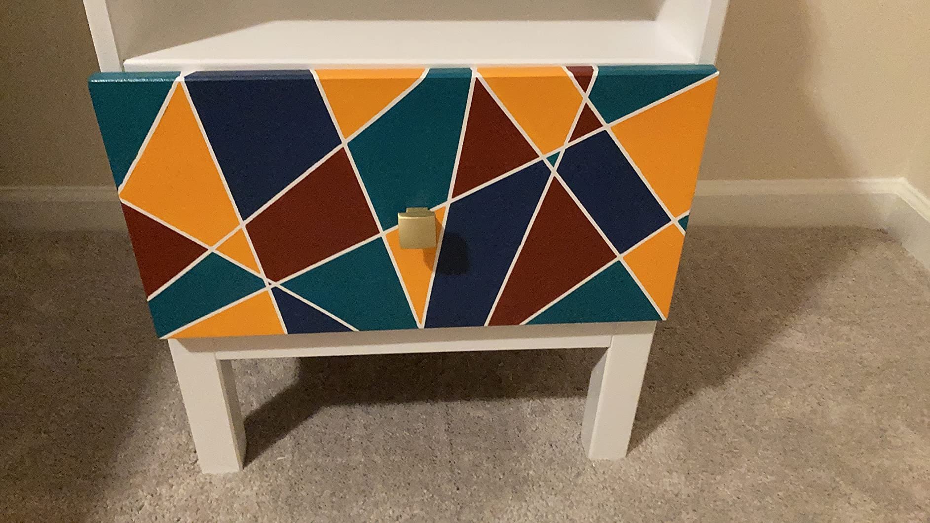 Drawer front with a geometric pattern of teal, orange, navy, and maroon shapes separated by white lines, with a gold knob.