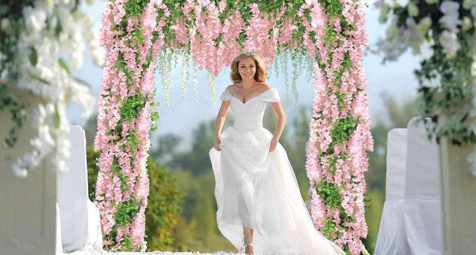 Bride walking through a pink wisteria floral archway decorated with white flowers