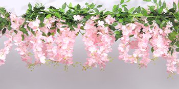 Close-up of a pink wisteria garland with green leaves, draped against a light gray background.