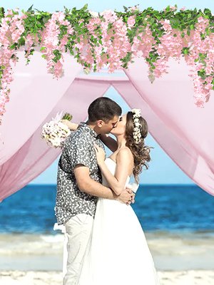 Wedding couple kissing under a pink wisteria floral arch on a beach