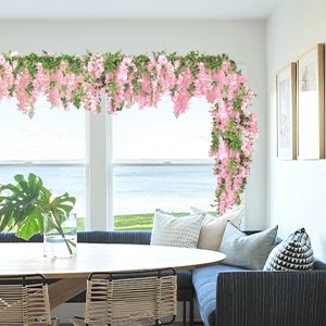 Pink wisteria garland with green leaves draped over a window and along a wall above a dining table.
