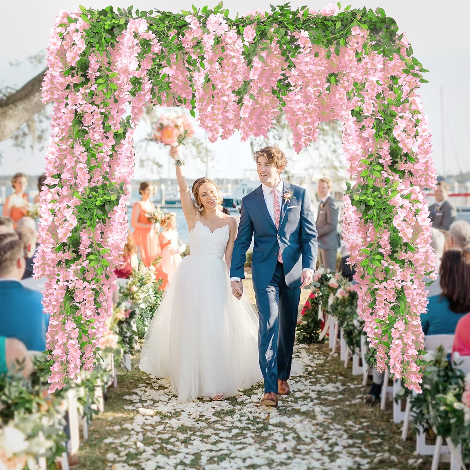Bride and groom walking down aisle under pink wisteria arch at outdoor wedding ceremony