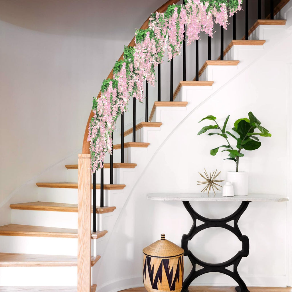 Pink wisteria garland draped over a staircase railing with green leaves