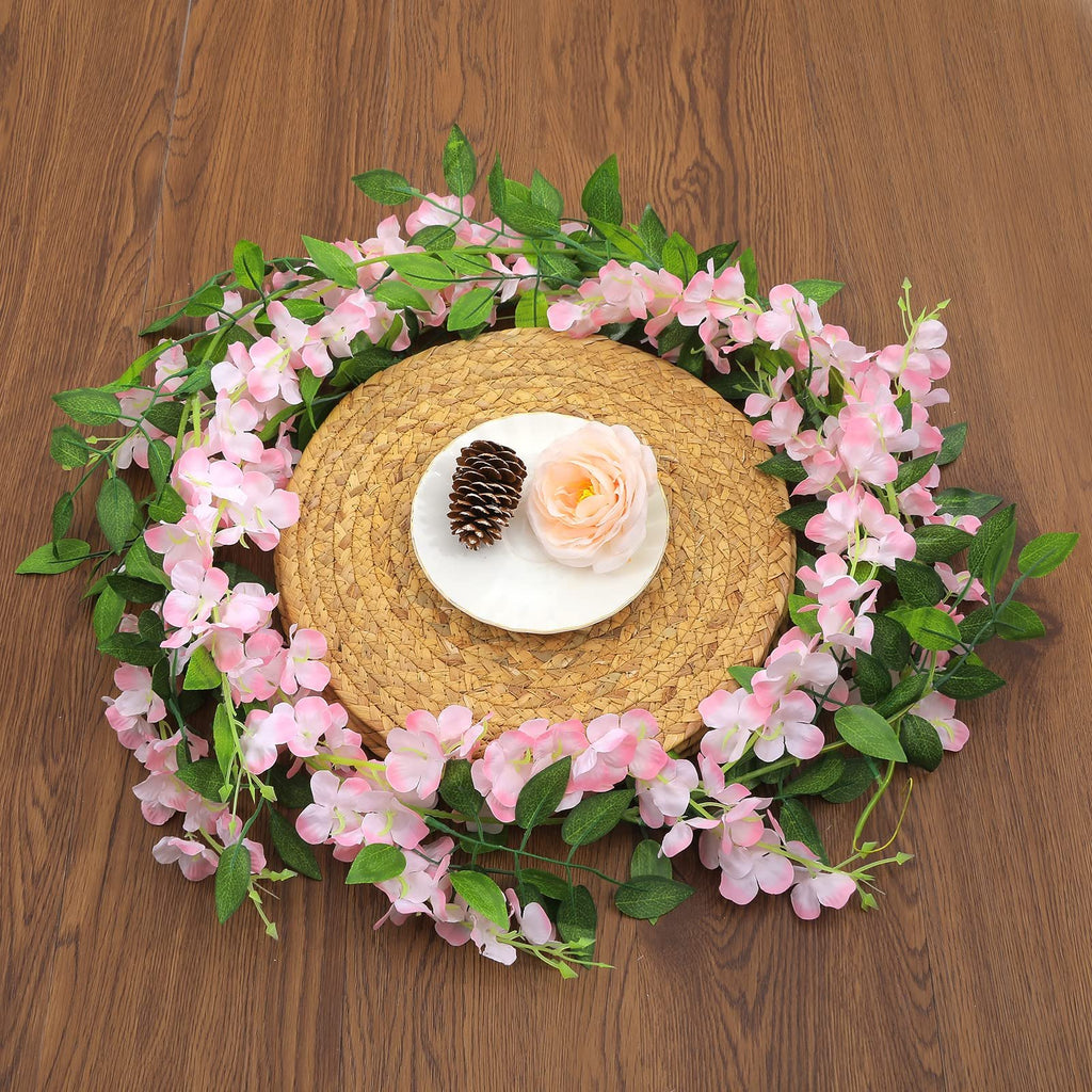 Pink wisteria garland arranged in a circle around a placemat with a pinecone and rose on a plate