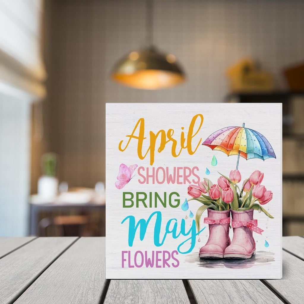 Wooden spring sign with text 'April Showers Bring May Flowers', featuring pink tulips in rain boots and a colorful umbrella.