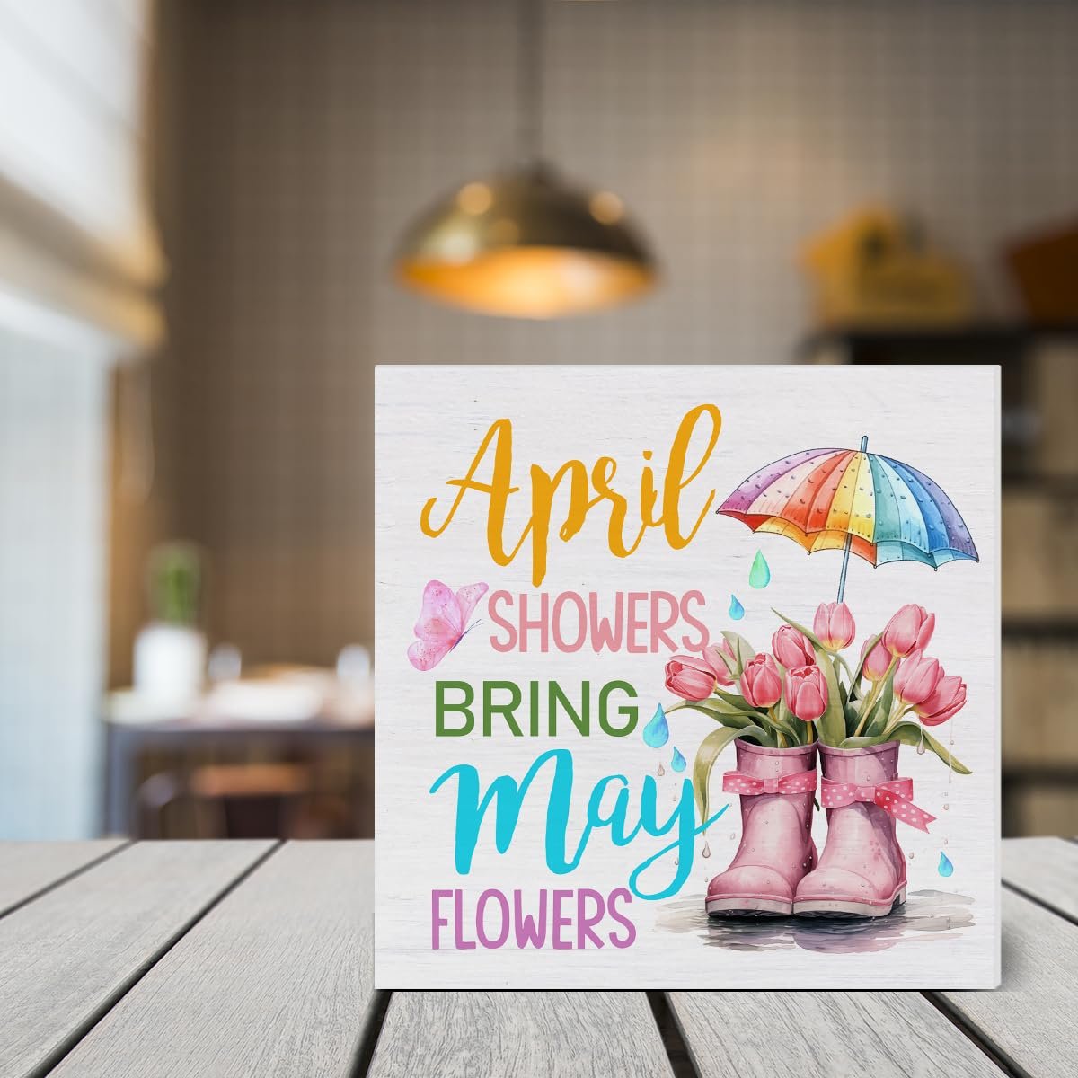 Wooden spring sign with text 'April Showers Bring May Flowers', featuring pink tulips in rain boots and a colorful umbrella.