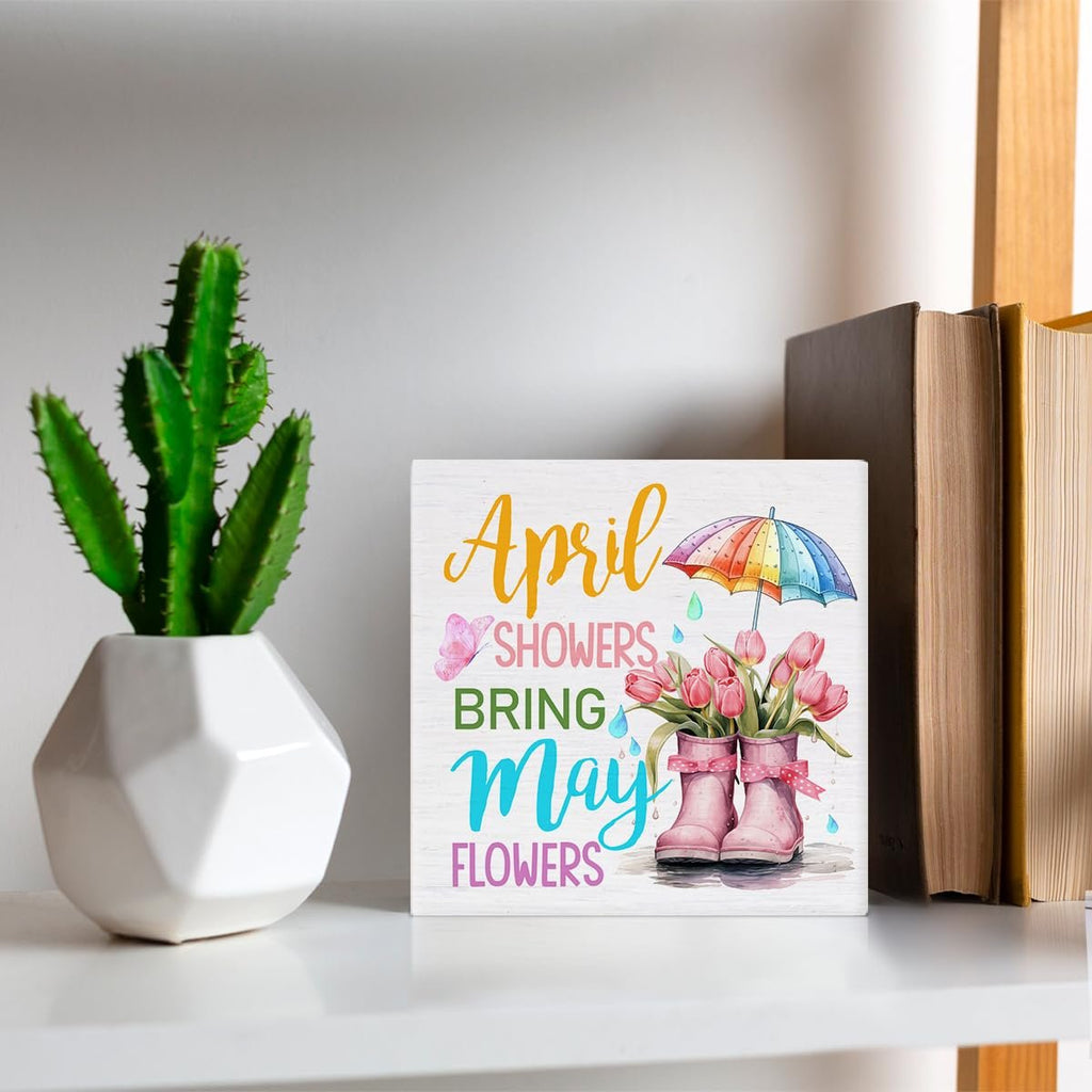 Wooden spring sign with pink tulips in boots, umbrella, and butterfly. Text reads 'April Showers Bring May Flowers'.