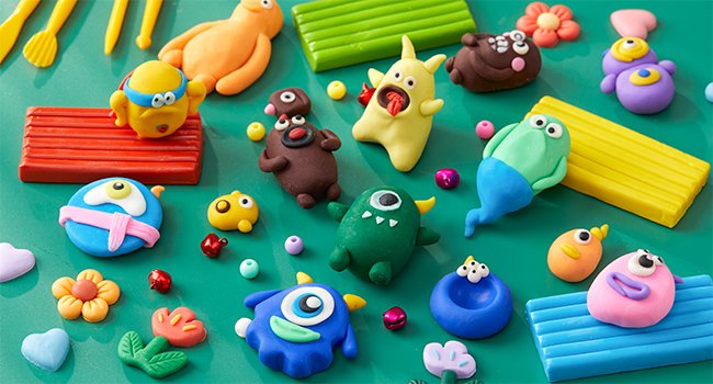 Various colorful polymer clay creations including monsters, flowers, and animals, with sculpting tools and clay blocks scattered on a green surface.