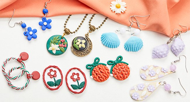 Assortment of handmade polymer clay jewelry including earrings, necklaces, and charms, displayed on a white surface with an orange fabric backdrop.