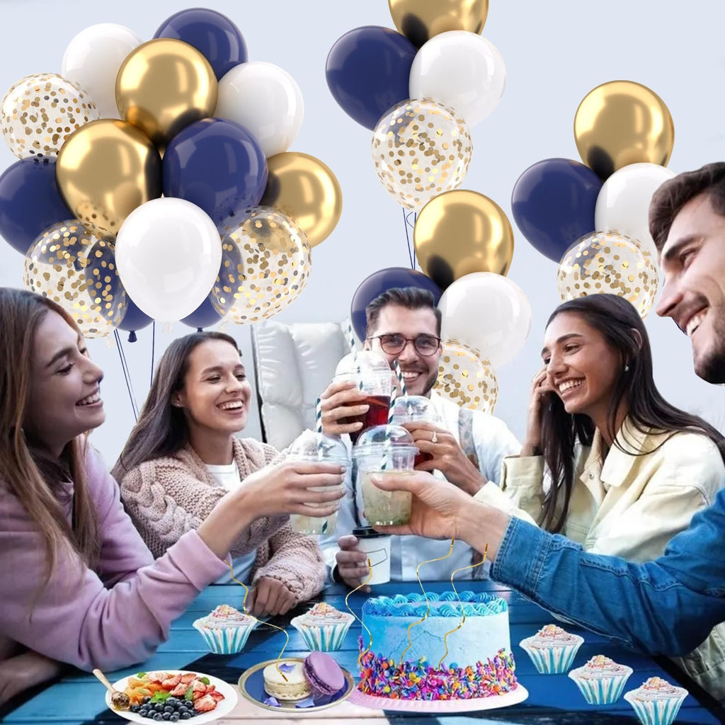 Group of friends toasting with drinks at a party with navy blue, gold, white, and confetti balloons overhead and a decorated cake on a table.