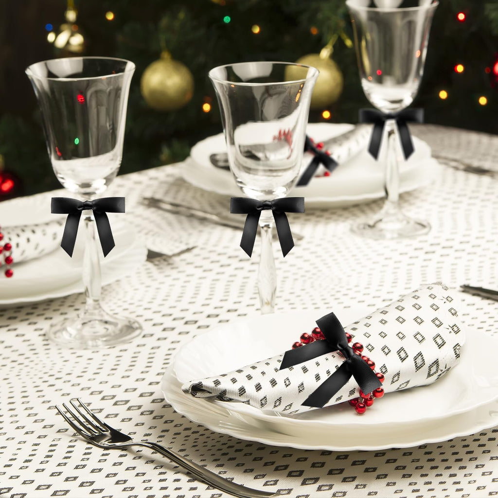Table setting with wine glasses, plates, and napkins decorated with black bows and red beads, with a Christmas tree in the background.