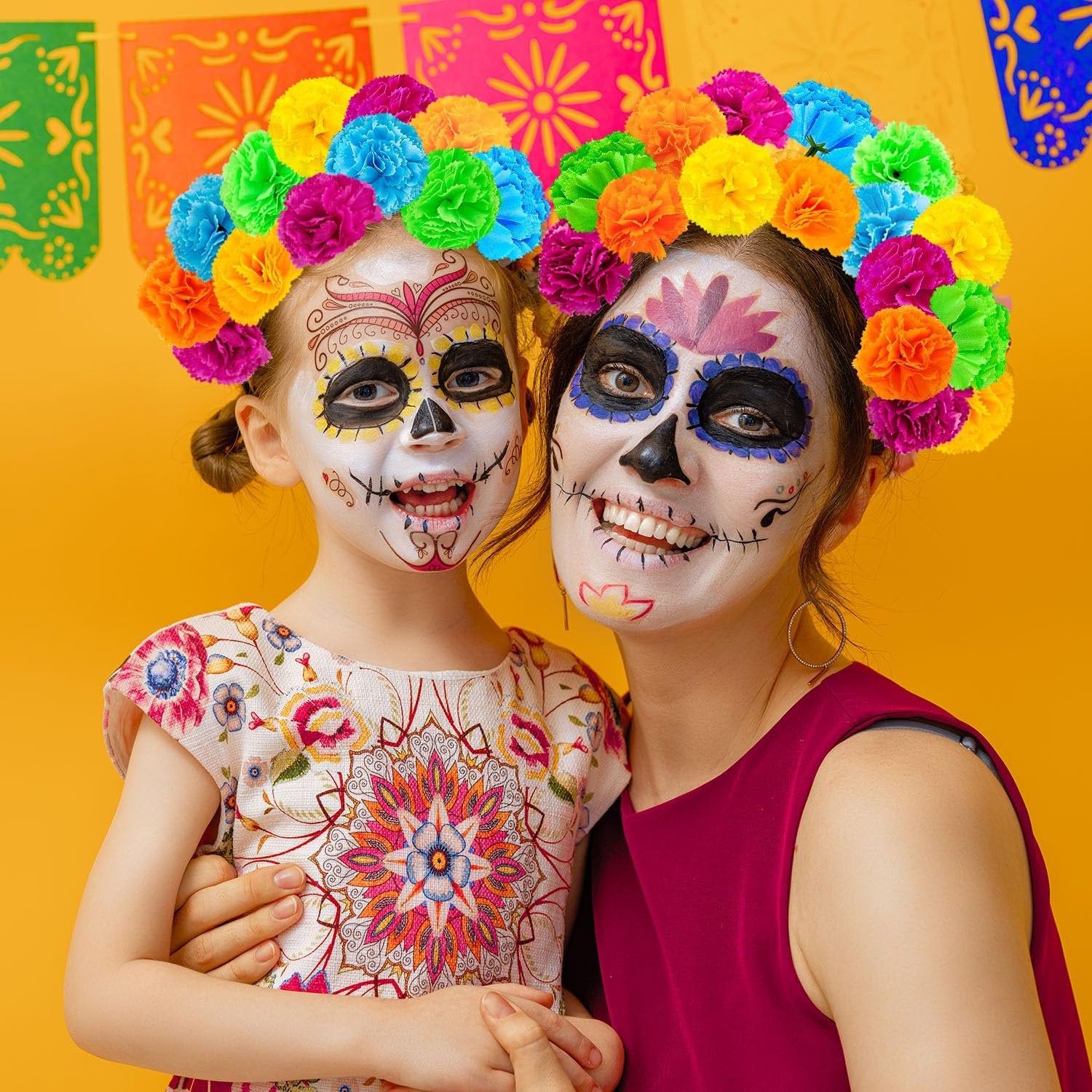 Mother and daughter with sugar skull makeup wear colorful marigold flower crowns against a yellow background with festive banners.