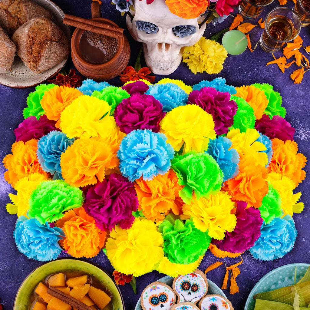 Assortment of colorful artificial marigold flower heads arranged on a dark surface with Day of the Dead themed items