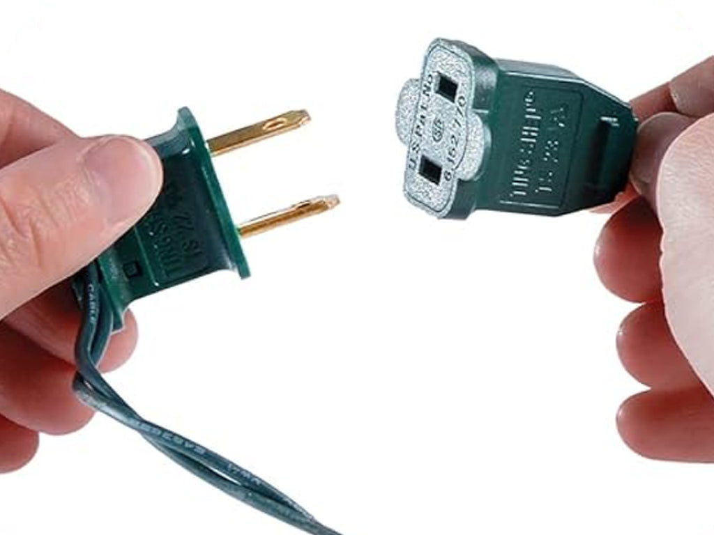 Close-up of hands connecting a green Christmas light plug and socket on a white background.