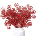A bunch of red glitter curly twig picks in a white vase against a white background.