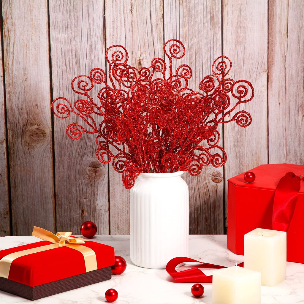 Red glitter curly twig picks in a white vase with Christmas decor, including gift boxes and candles.