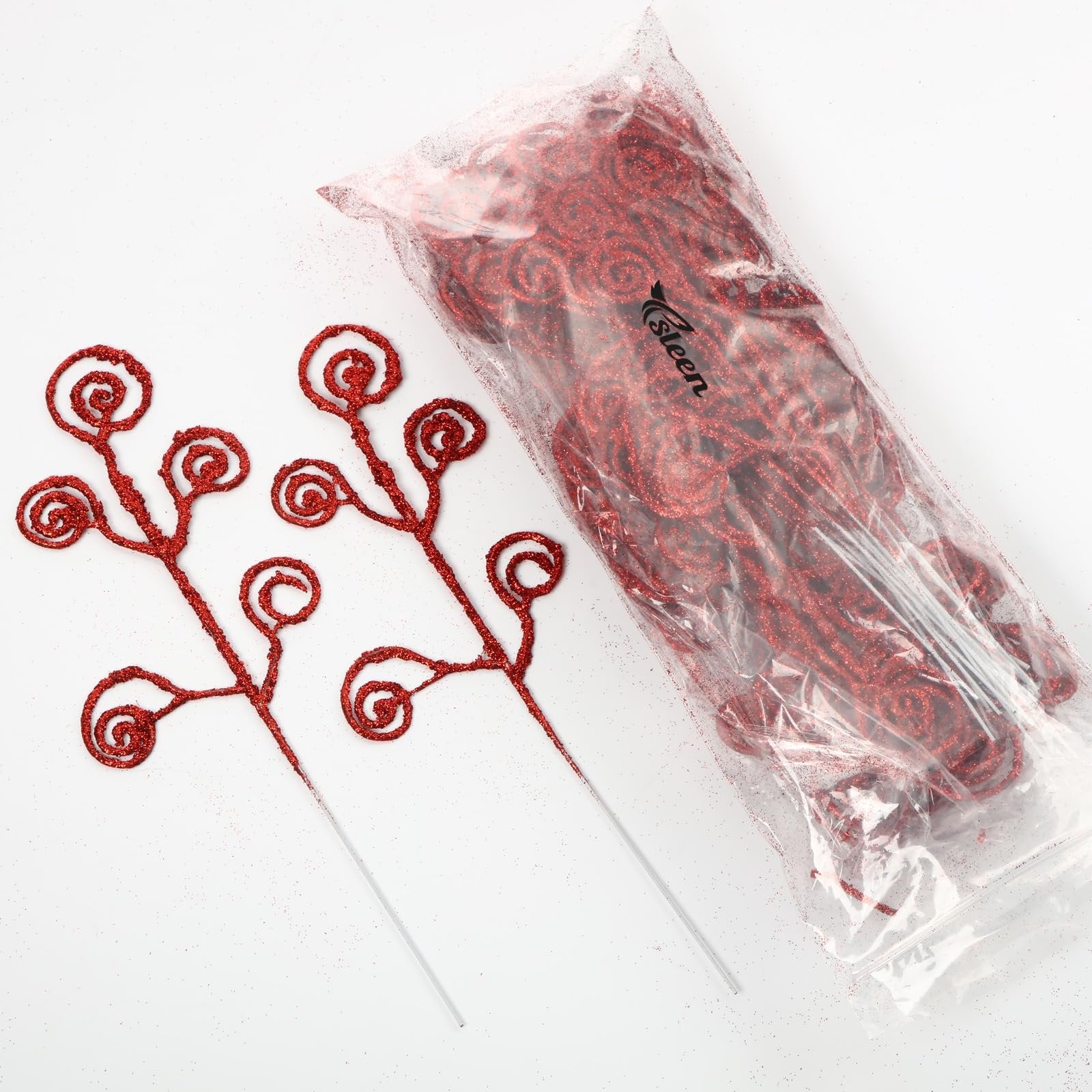 Two red glitter curly twig picks next to a clear plastic bag filled with more red glitter curly twigs on a white background.