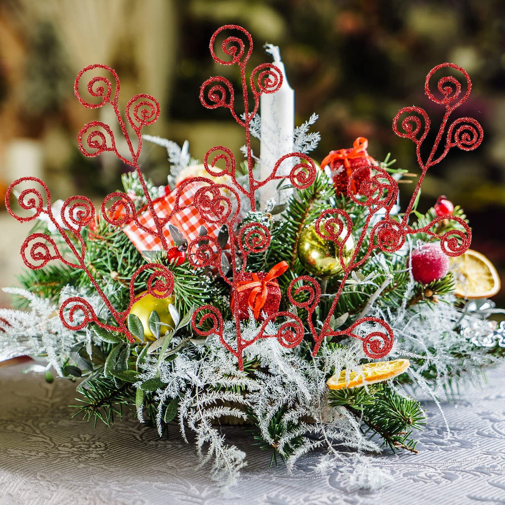 Christmas centerpiece with red glitter curly picks, pine branches, ornaments, and dried orange slices on a table.