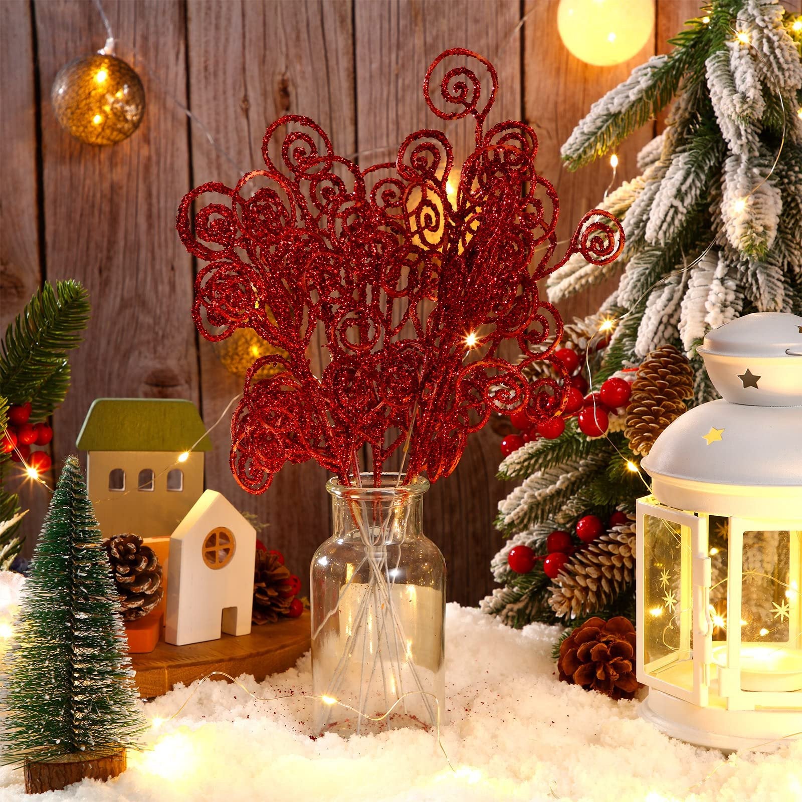 Red glitter curly tree picks in a glass vase with a snowy Christmas scene backdrop