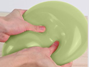 Hands squeezing a light green slime on a wooden surface