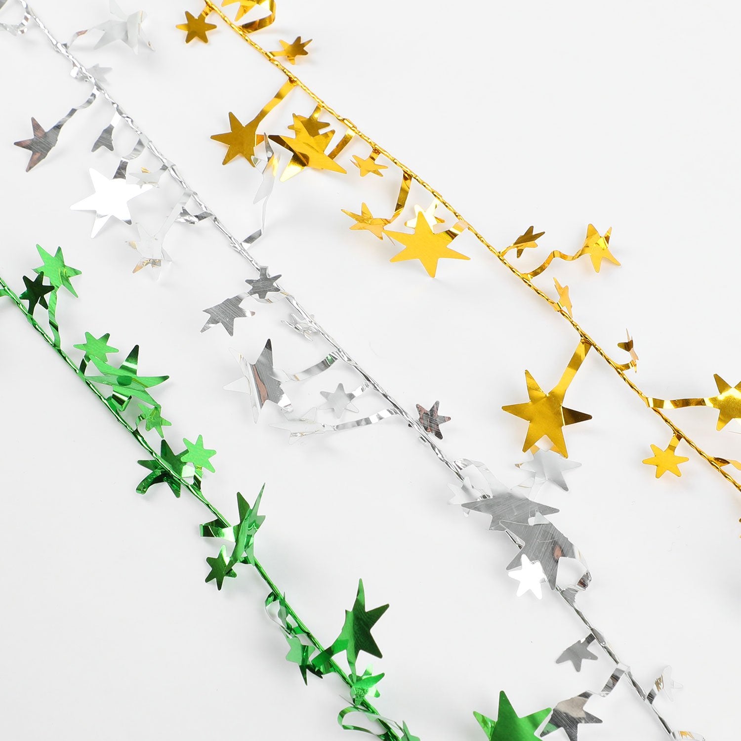 Three strands of star tinsel garland in gold, silver, and green, laid diagonally on a white background.