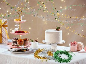 Christmas party table setting with cake, cupcakes, pastries, and tinsel garland decorations.