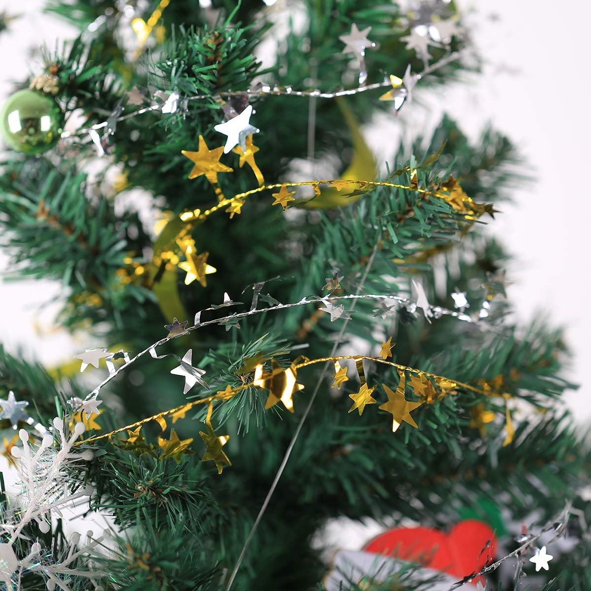 Close-up of gold and silver star tinsel garland draped on a green Christmas tree with a green ornament.