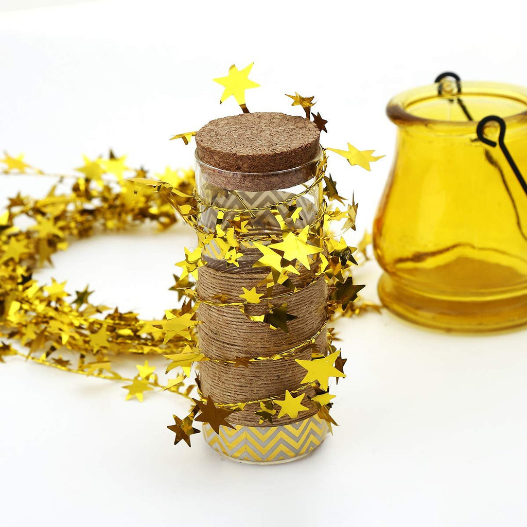 Gold star tinsel garland wrapped around a glass jar with twine and a yellow glass lantern in the background.