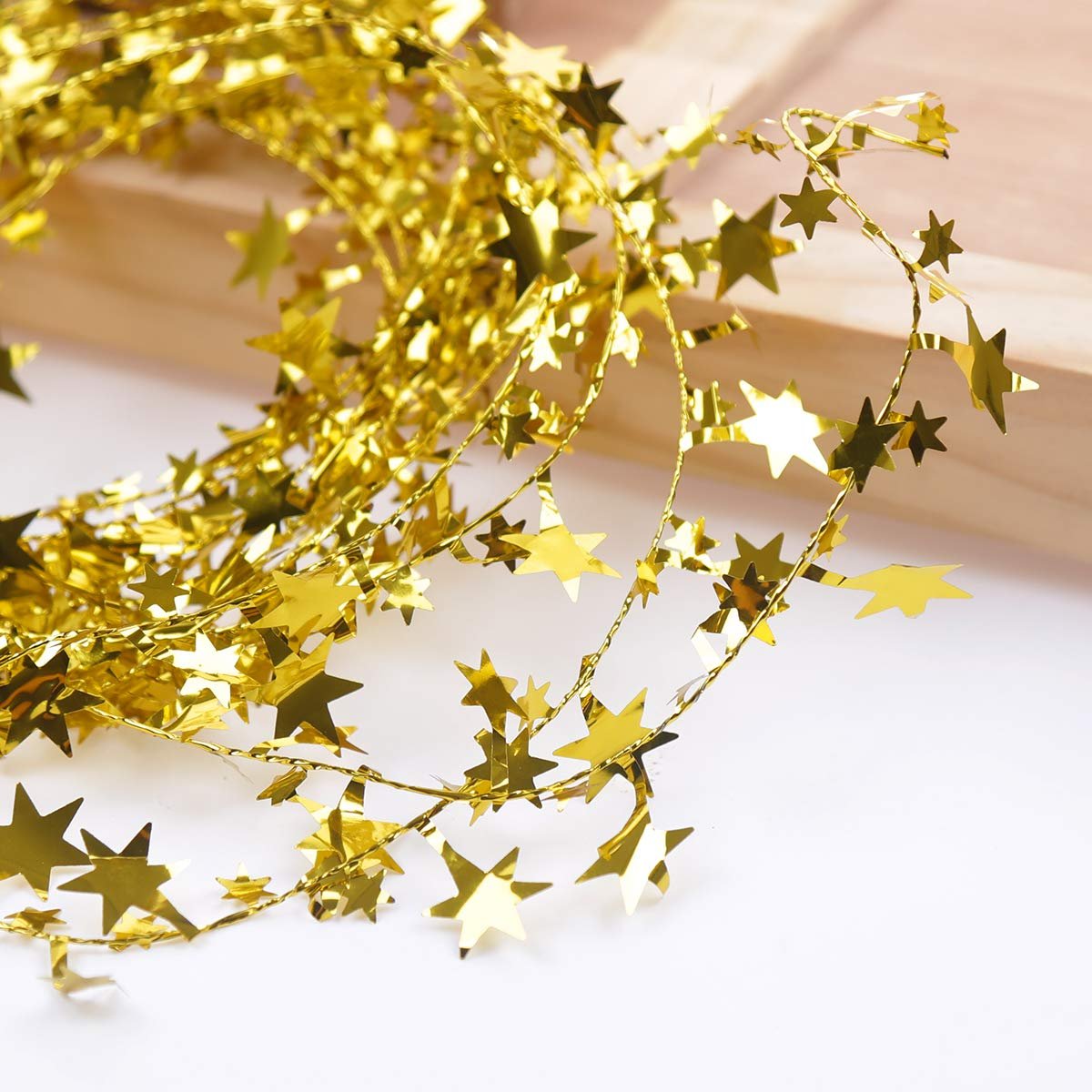 Close-up of a gold tinsel wire garland with star-shaped cutouts, draped on a white surface with a wooden background.