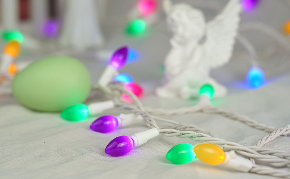 Multicolor Easter string lights with white wire, a green egg, and a white angel figurine.