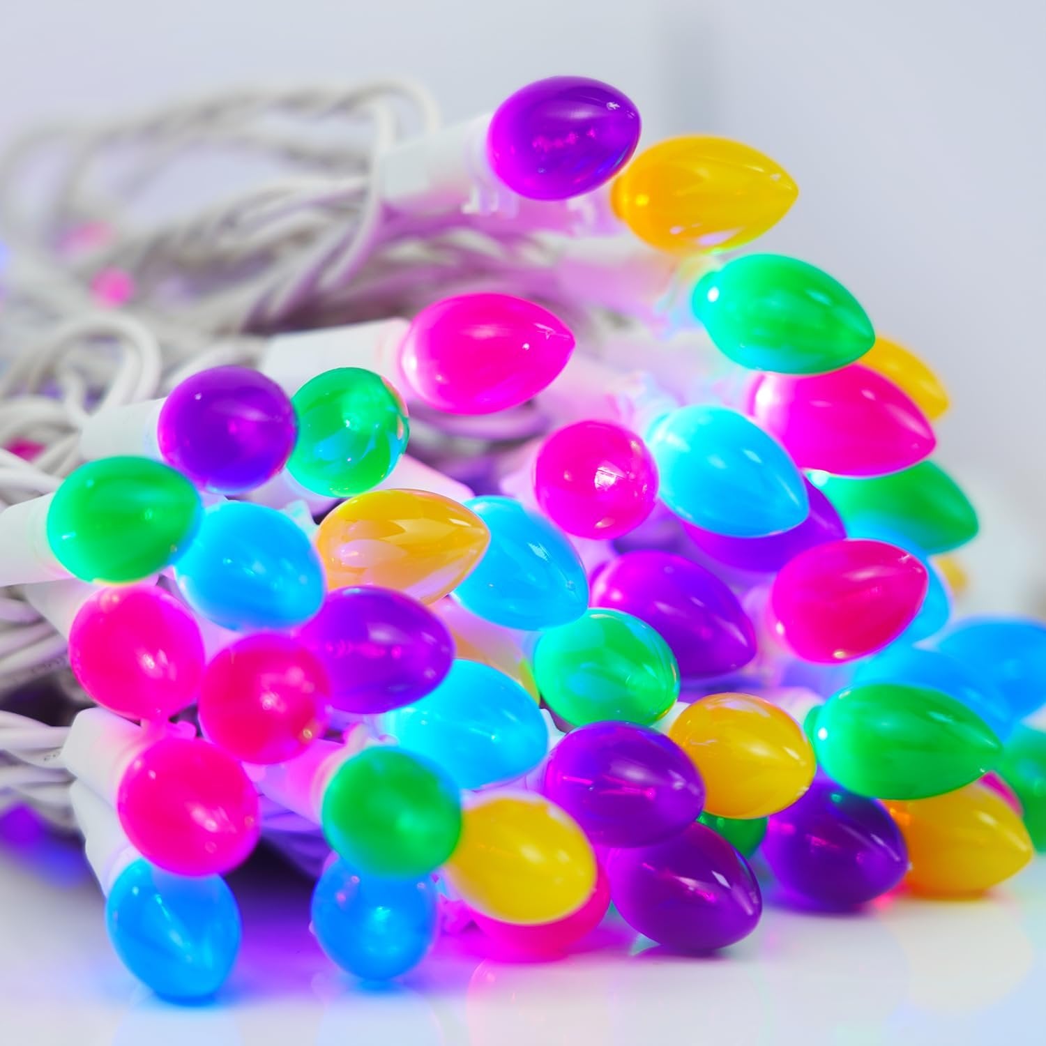 Close-up of a pile of multicolor LED string lights with white wire, featuring purple, green, blue, yellow, and pink bulbs.