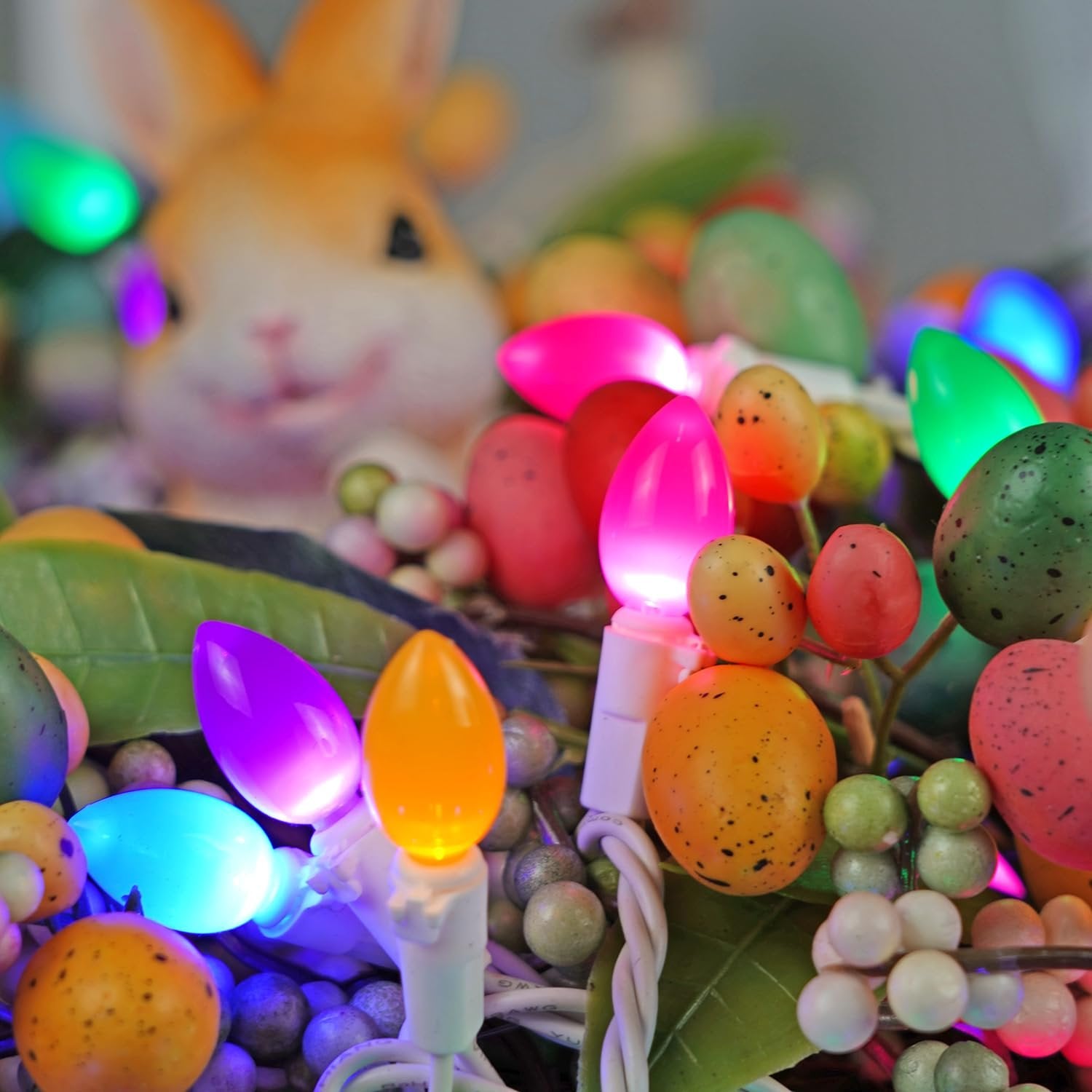 Close-up of multicolor Easter string lights with a blurred bunny figure in the background.