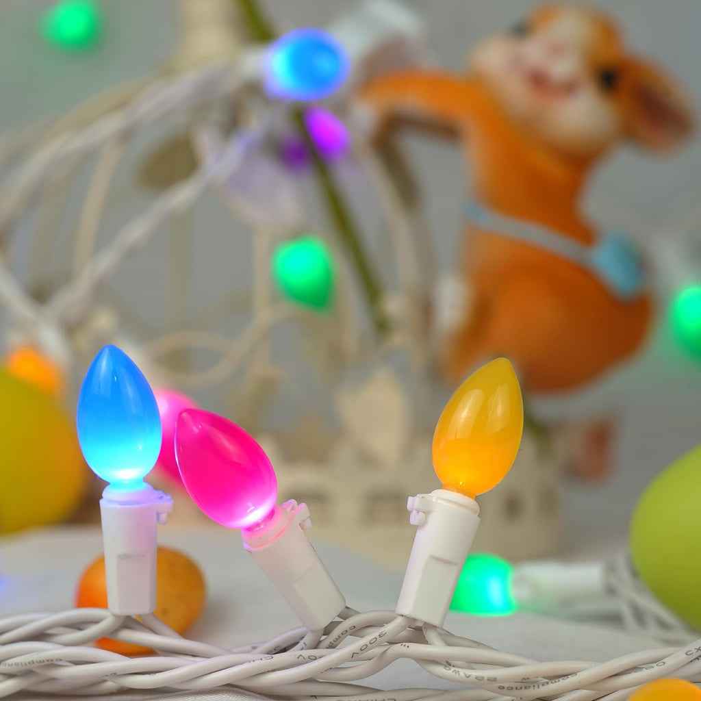 Close-up of multicolor LED string lights with blue, pink, and yellow bulbs illuminated, set against a blurred background with a decorative Easter figurine.