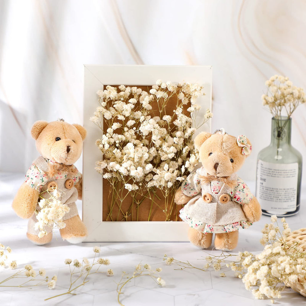 Two teddy bears and dried baby's breath flowers arranged with a white frame and a glass vase.
