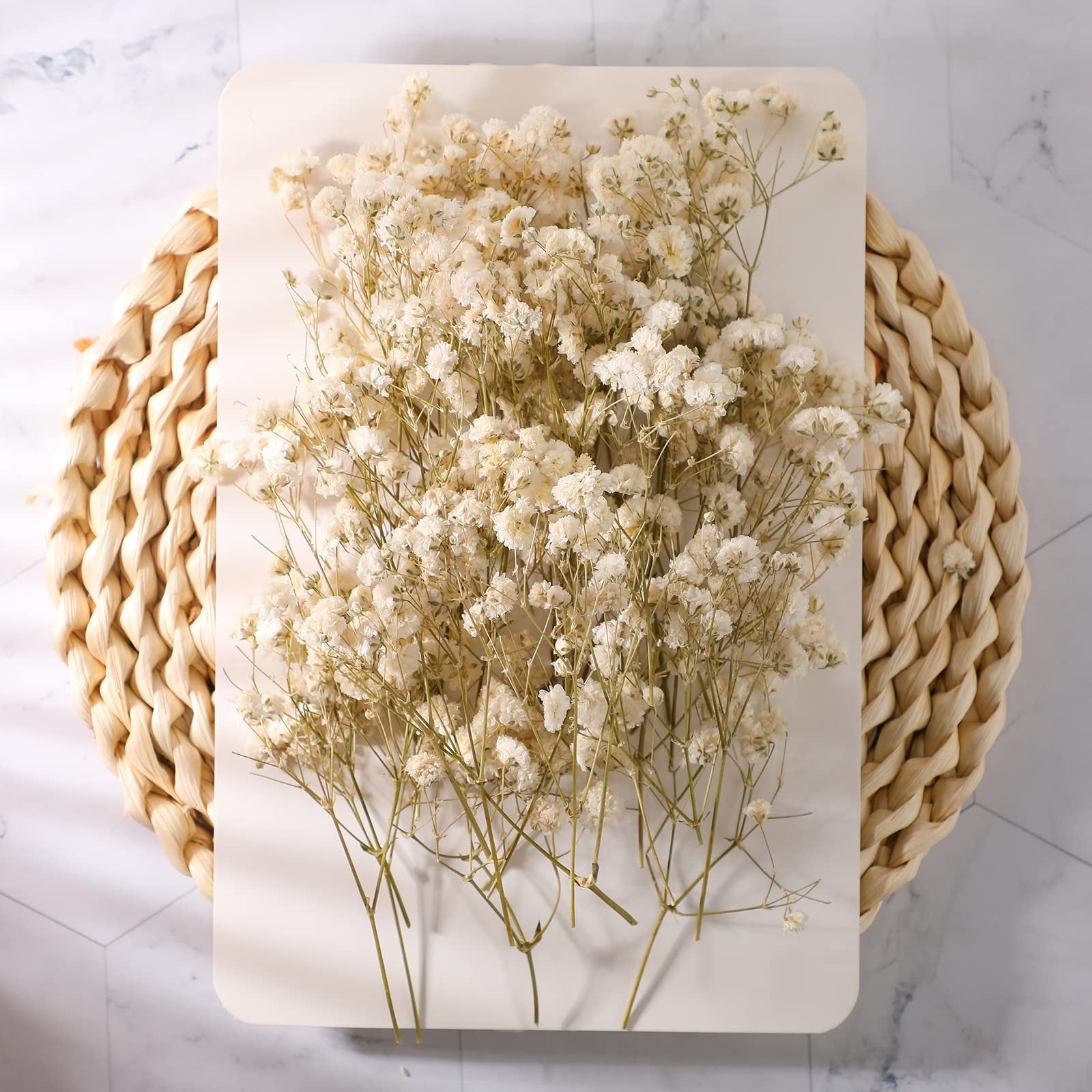 Ivory dried baby's breath flowers arranged on a white card, with a woven placemat and marble background.