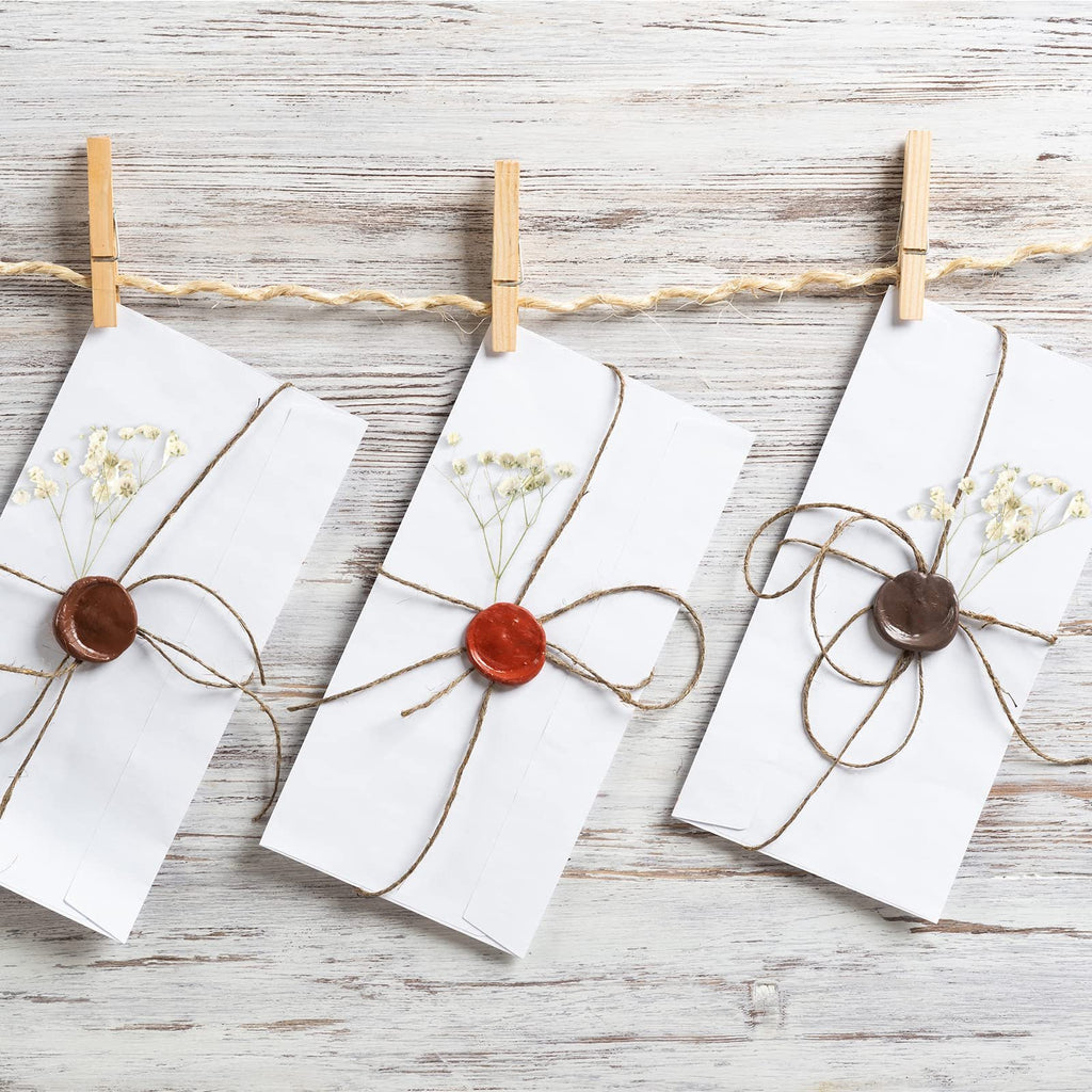 Three white envelopes with dried baby's breath and wax seals hanging on a twine clothesline